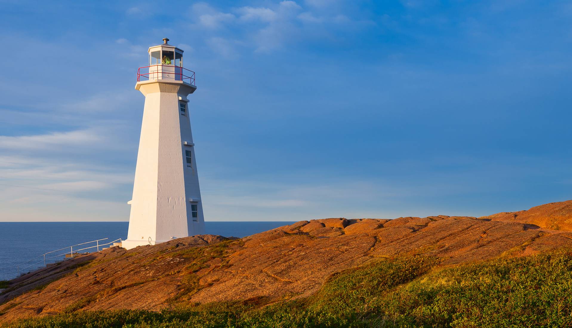 lighthouse in Newfoundland with ocean in background, rocks in foreground