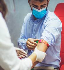 man wearing mask with sleeve rolled up and health-care professional inserting needle